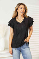 Model wearing a black eyelet flutter sleeve top with tie-neck, styled with denim jeans.
