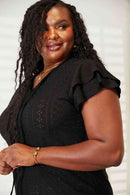 Curvy model wearing an eyelet flutter sleeve top, showcasing elegant tie-neck design and delicate flutter sleeves.