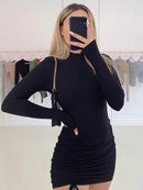 Black turtleneck bodycon mini dress on a model, showcasing long sleeves and a ruched design.