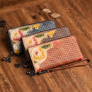Hand-painted leather clutch purse in three colors with floral designs on a wooden surface.