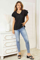 Model wearing an eyelet flutter sleeve top with tie-neck, paired with jeans and stylish heels.