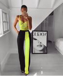 Model wearing floral lace bodysuit lingerie with neon accents and black pants, standing in modern interior.