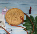 Colorful straw bucket bag on a blue wooden table next to cosmetics and greenery.