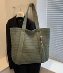 Fashion straw shoulder bag in green with tassel design, displayed on a hanger.
