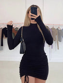 Black turtleneck bodycon mini dress with long sleeves, featuring ruched detailing, worn by a woman in a mirror.